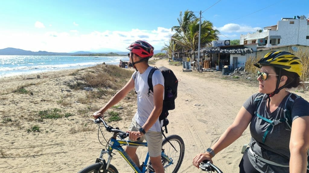 Two people standing with bikes and beach in the background