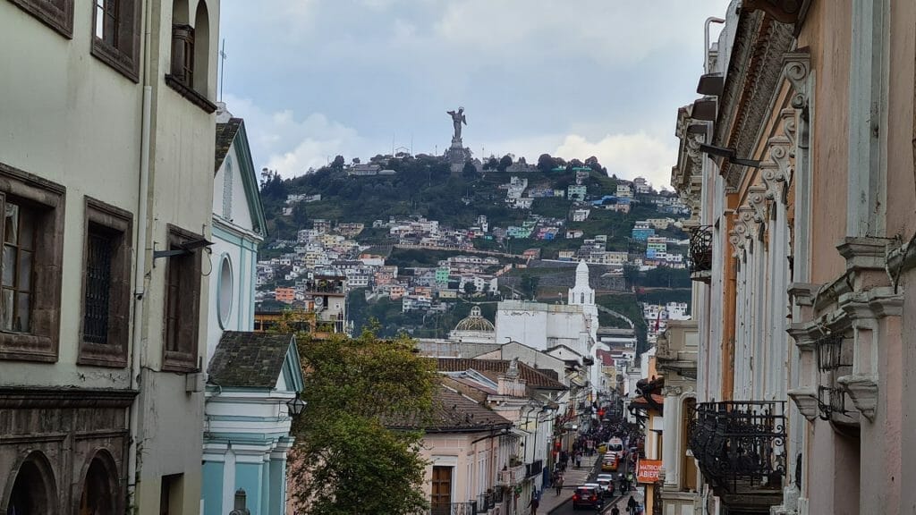 View of narrow street in Quito with angel statue in background