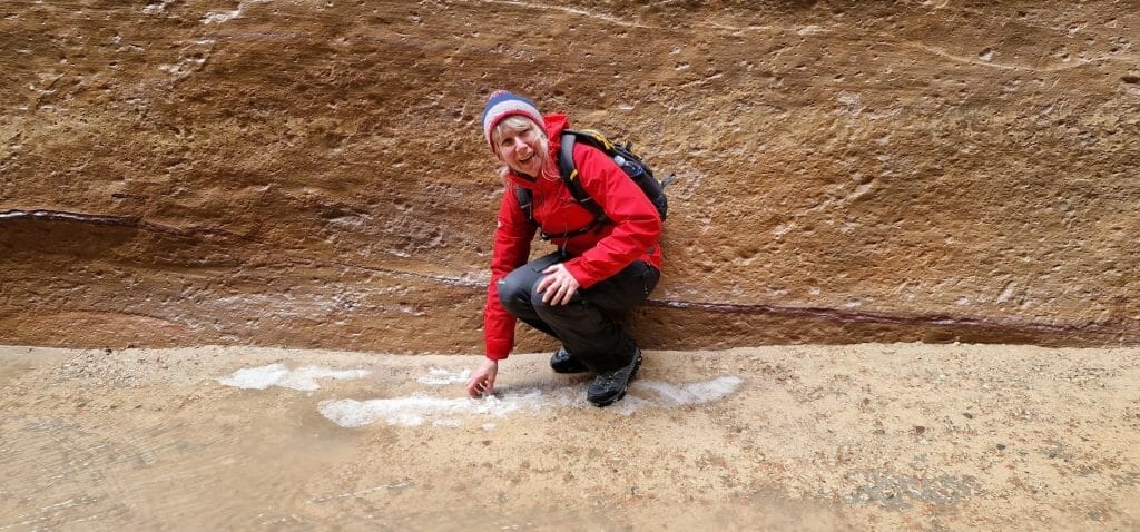 Jane kneeling down to touch pile of hailstones inside Petra