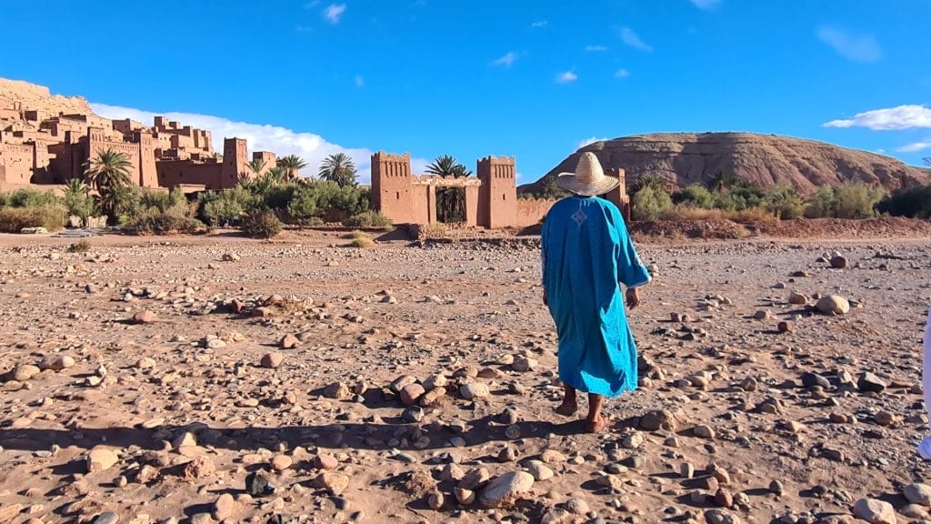 Guide on dry river bed with castelated gate of ksar ait ben haddou in background
